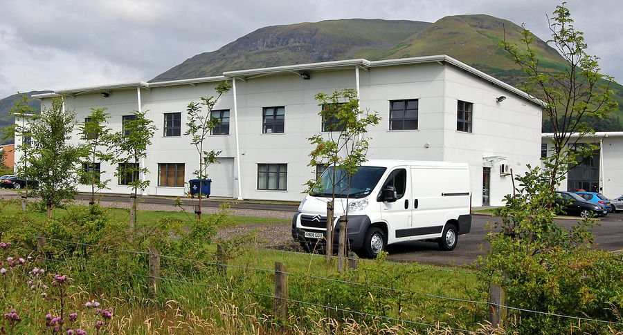 A white modern office building with private car parking in front and the Ochil Hills behind